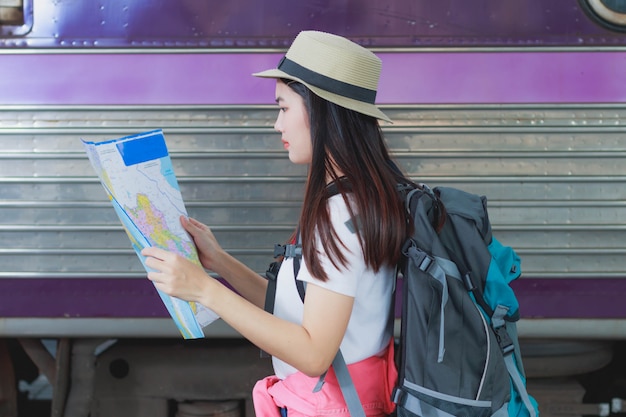 鉄道駅の地図を運ぶバックパックを運ぶ美しい女性。