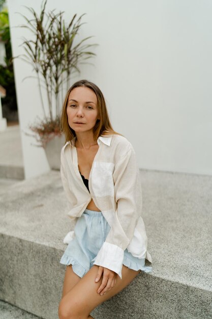 Bella donna in camicetta bianca casual in posa sulla strada sopra il muro bianco