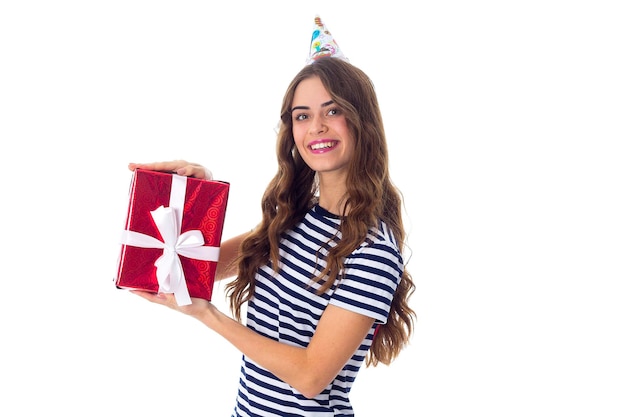 Beautiful woman in celebration cap holding red present with white ribbon and opening it