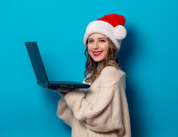 Beautiful woman in Christmas hat with laptop computer on blue wall