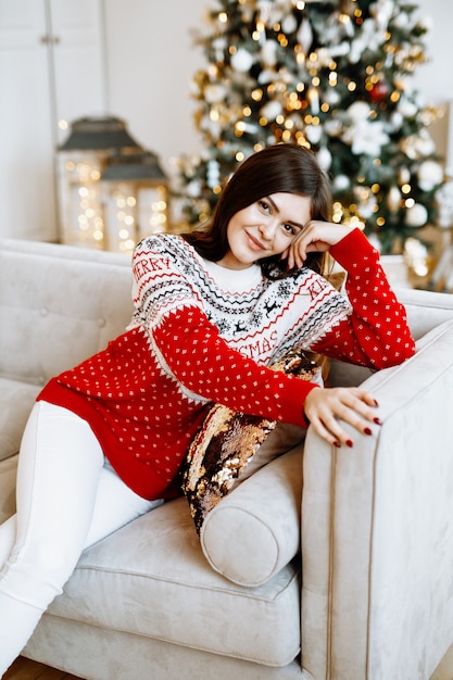 Foto una bella donna in un maglione di natale posa contro un abete decorato