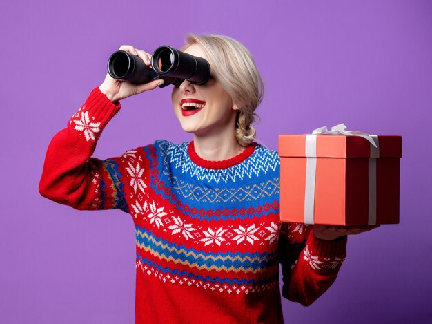 Beautiful woman in Christmas sweater with gift box and binocular  