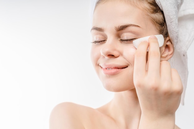 Photo beautiful woman cleaning her face with cotton swab - over white background and smiling