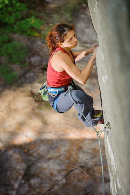 Beautiful woman climber climbing steep rock with rope