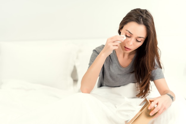 Beautiful woman crying in bed and using tissues