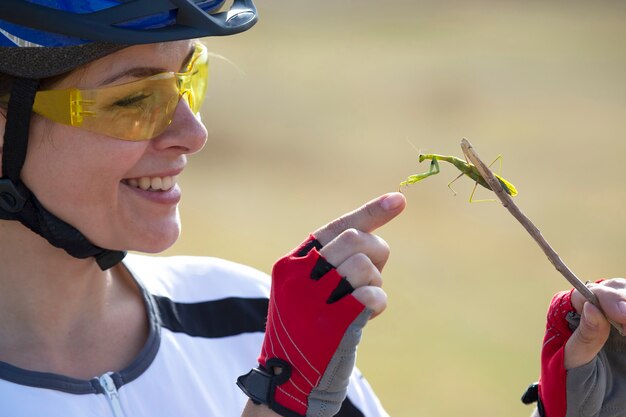 Beautiful woman cyclist holding a mantis beetle. Nature and woman