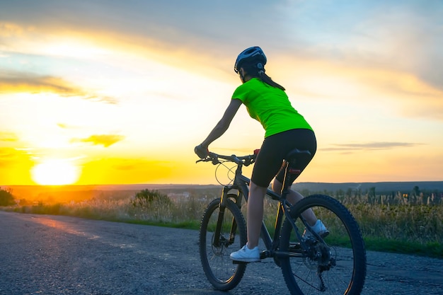 Beautiful woman cyclist rides a bicycle on the road in the sunset. Healthy lifestyle and sport. Leisure and hobbies