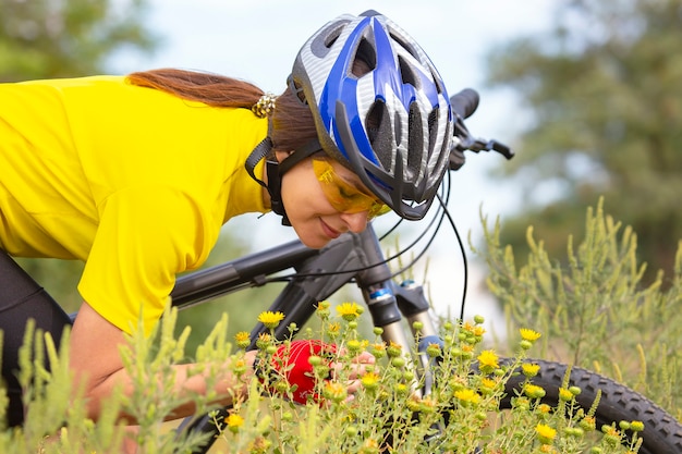 花を嗅ぐ黄色いフィールドの美しい女性サイクリスト。スポーツとレクリエーション。自然と人間