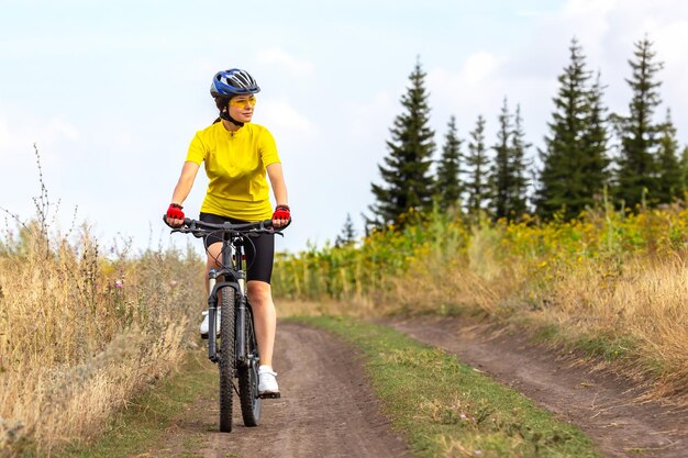 黄色いシャツを着た美しい女性サイクリストがフィールド・ロード・スポーツに沿って自転車に乗っています