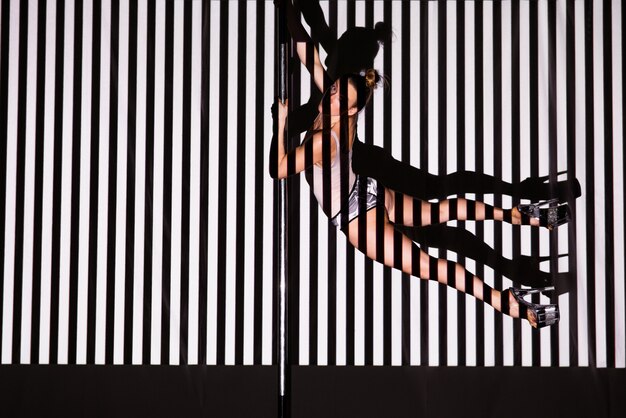 Photo beautiful woman dances near a pole on a striped wall