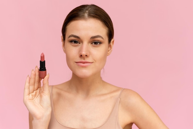 Beautiful woman demonstrating lipstick while standing at isolated pink background