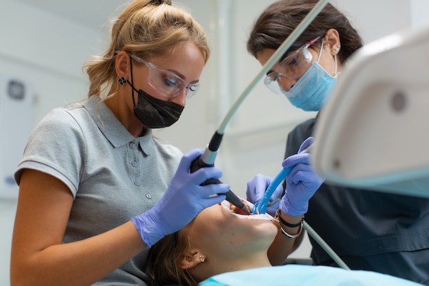 Красивая женщина-стоматолог в защитных очках лечит зубы пациента