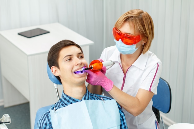 Beautiful woman dentist treating a patient teeth in dental office. Doctor wearing glasses, mask, white uniform and pink gloves. Dentistry