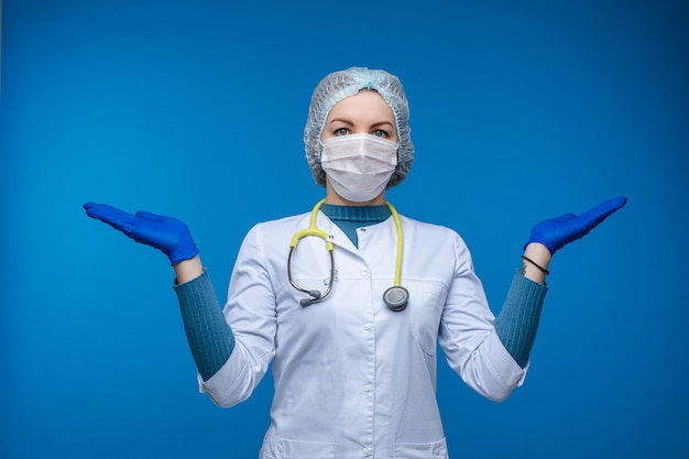 Beautiful woman doctor in white medical clothes, mask, phonendoscope and medical hat doesn't know what to do