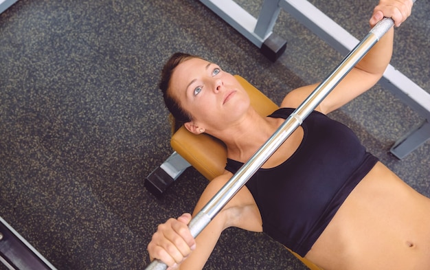 Beautiful woman doing exercises with barbell on a bench press training in a fitness center