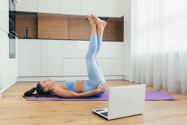 Bella donna facendo fitness a casa in linea con il computer portatile