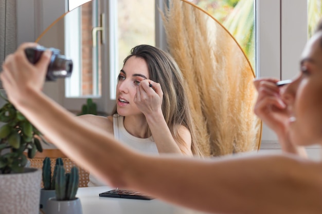 Beautiful woman doing her mekup while vlogging cosmetic review holding camera