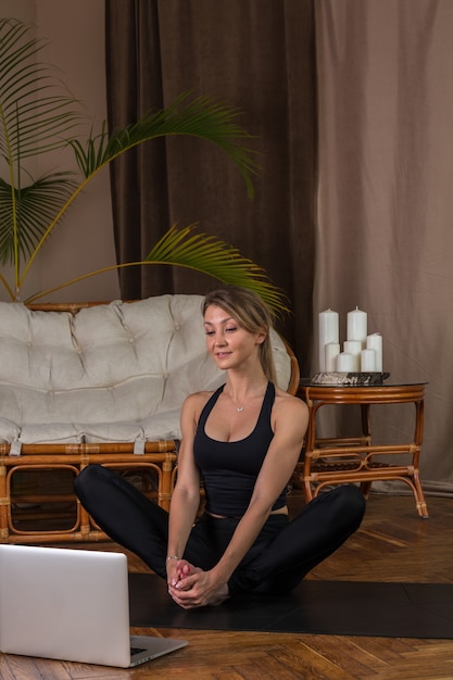 Bella donna che fa pilates su un tappetino a casa guardando l'allenamento online sul computer portatile