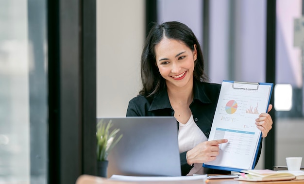 Beautiful woman doing video conference online via laptop computer presenting business growth graph and discussing with her colleague at office