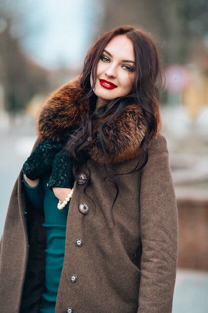 Beautiful woman in a dress and coat with a fur collar. Elegant bright make-up, red lips, looking