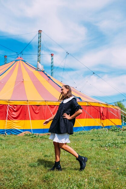 Foto bella donna in abito posa sullo sfondo di una tenda da circo in una giornata di sole