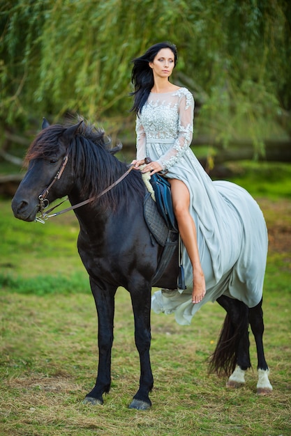 Beautiful woman in dress with black horse in nature