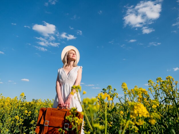 Beautiful woman in dress with suitcase in rapeseed field