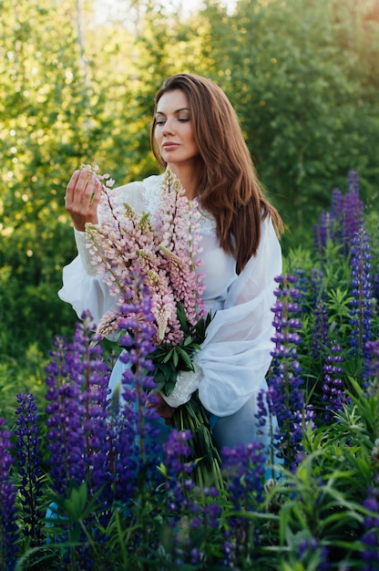 Beautiful woman dressed in a dress in flowers lupines at sunset