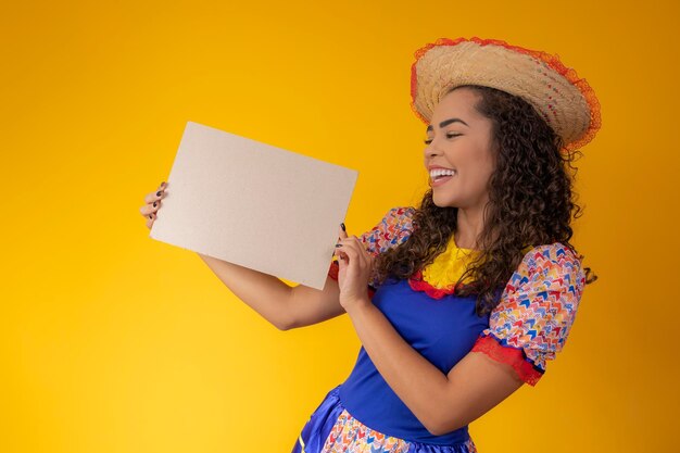 Beautiful woman dressed in festa junina outfit holding a blank sign with copy space