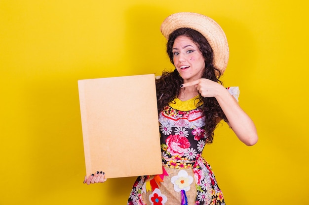 Beautiful woman dressed in typical clothes for a festa junina holding sign for text or ad advertisement