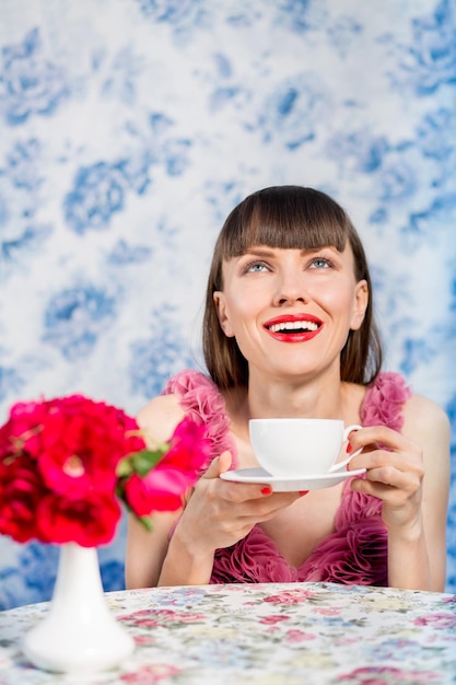 青い花の背景の上に熱いお茶を飲む美しい女性
