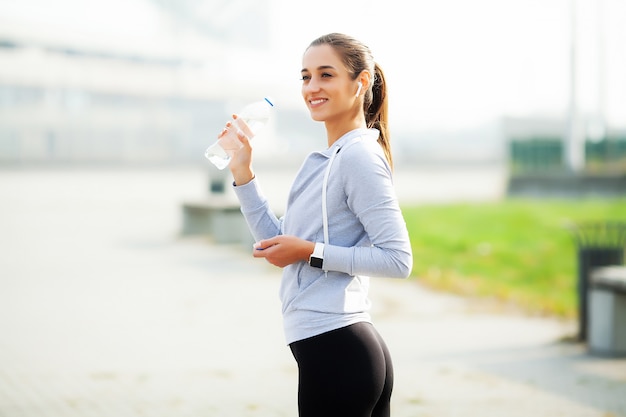 Beautiful woman drinking water and listen to music after running