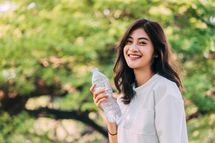 美しい女性は夏緑公園で水を飲む。健康的なライフスタイルのコンセプト