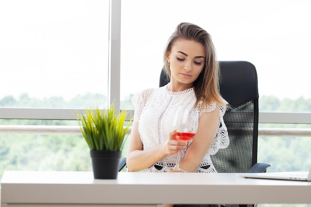 Bella donna beve vino sul posto di lavoro in ufficio