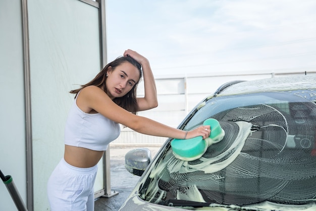 Beautiful woman driver at manual car service wash, use sponge white foam to clean dirt her auto