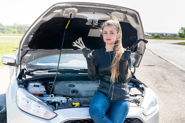 Beautiful woman driver with wrenches sitting on broken car