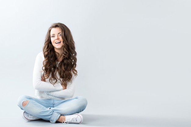 Beautiful woman on empty wall smiling and sitting on floor