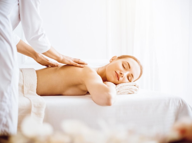 Beautiful woman enjoying back massage with closed eyes in sunny spa center Relaxing treatment concept in medicine