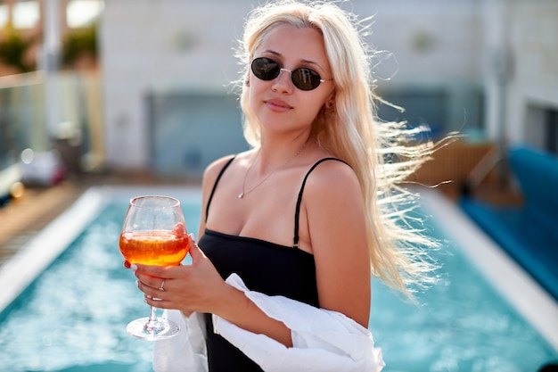 カクテルイタリアンaperol spritz付きのスイミングプールで楽しむ美しい女性。暑い晴れた日にプールでリラックスした女の子。