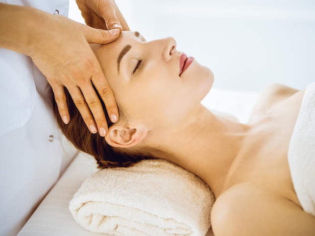 Beautiful woman enjoying facial massage with closed eyes in spa center. Relax treatment concept in medicine.