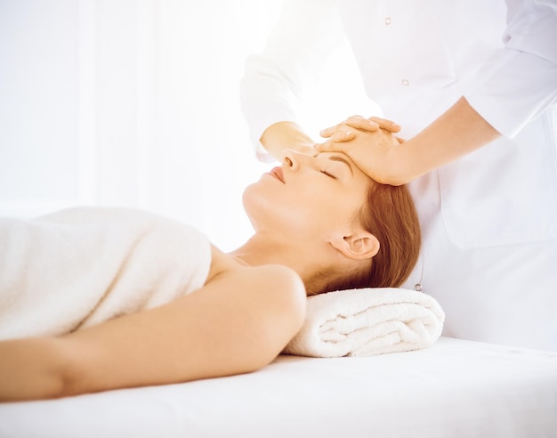 Beautiful woman enjoying facial massage with closed eyes in sunny spa center