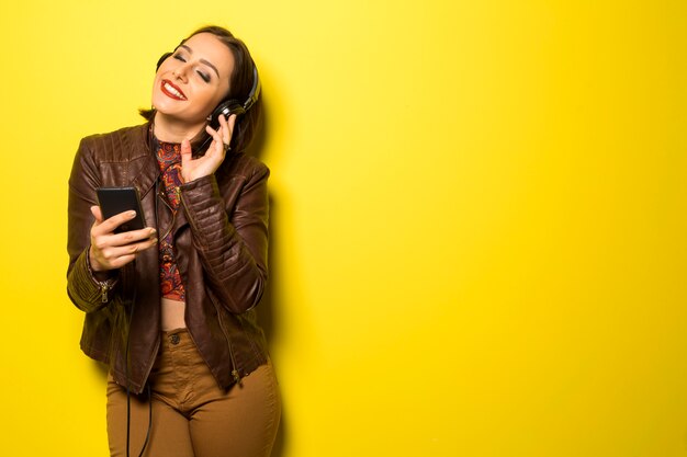 Beautiful woman enjoying music with the head phones in yellow wall