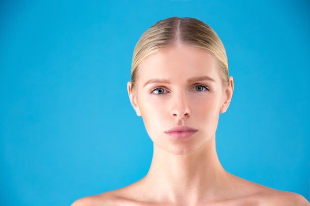 Beautiful Woman Face. Beauty Portrait of young woman blonde on blue background. Perfect Fresh Skin. Youth and Skin Care Concept.