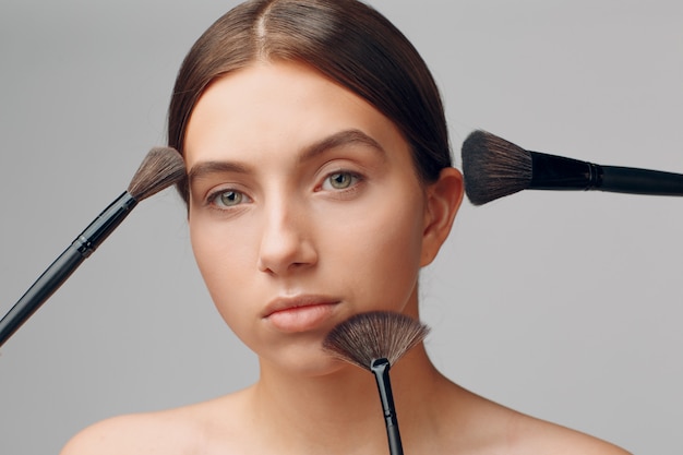 Volto di donna bella con il trucco naturale. mano del maestro del trucco con pennello. modello di bellezza giovane femmina. trucco in corso.