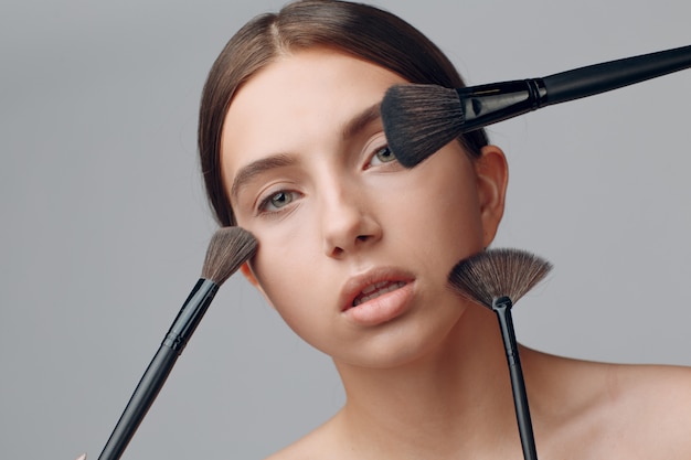beautiful woman face with natural makeup. hand of make-up master with brush. young beauty model female. make up in process.