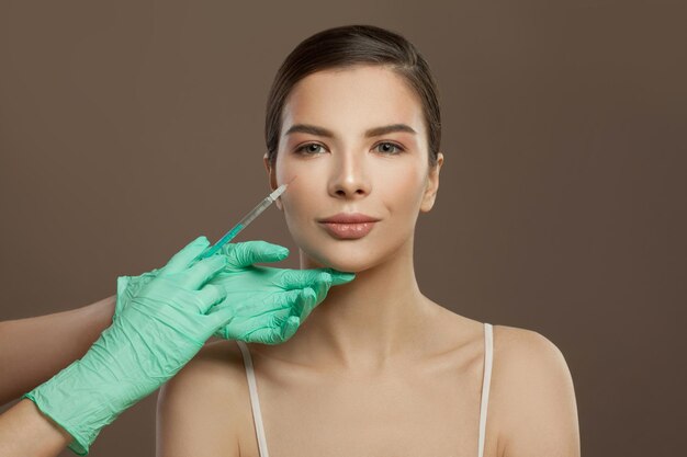 Beautiful woman face with syringe injection on brown background Cosmetologyconcept