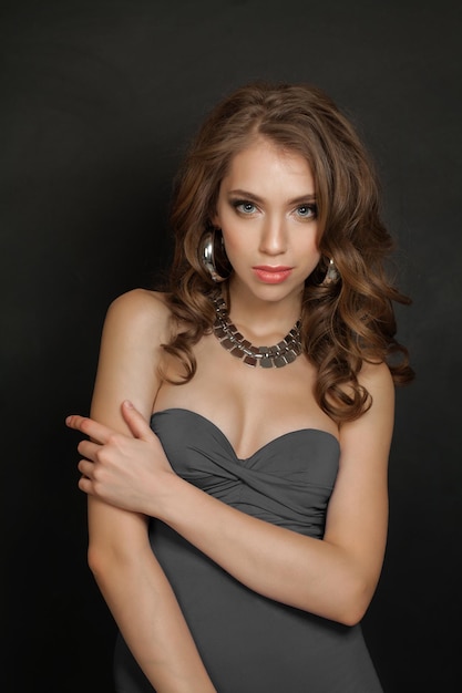 Красивая женщина-модель со здоровыми каштановыми волосами и серебряным ожерельем на черном фоне