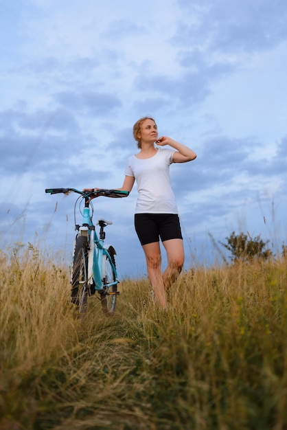 Una bella donna in campo con la sua bicicletta guardando il tramonto