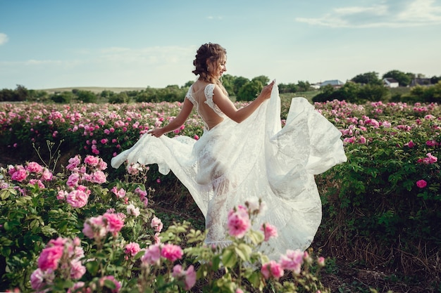 Beautiful woman in a floral park, garden roses. Makeup, hair, a wreath of roses. Long Wedding Dress. Woman in Boho style