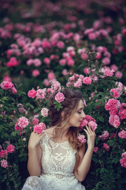 Beautiful woman in a floral park, garden roses. Makeup, hair, a wreath of roses. Long Wedding Dress. Woman in Boho style